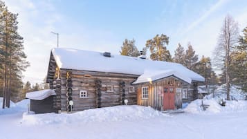 Une cabane en rondins dont le toit est recouvert de neige, entourée d’arbres.