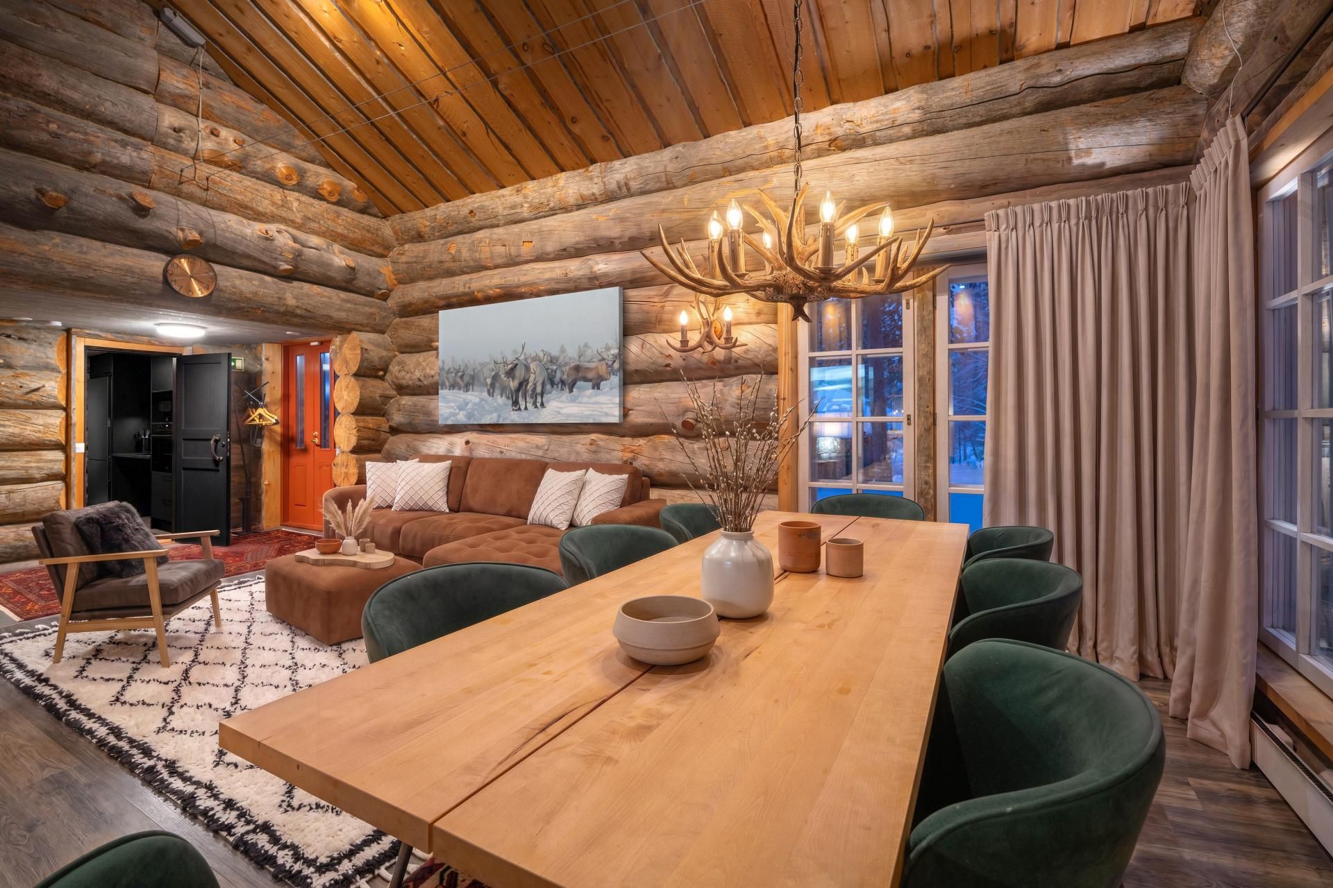 Ein Holzblockhaus-Interieur mit Esstisch, Stühlen, einer Couch und einem Kronleuchter.