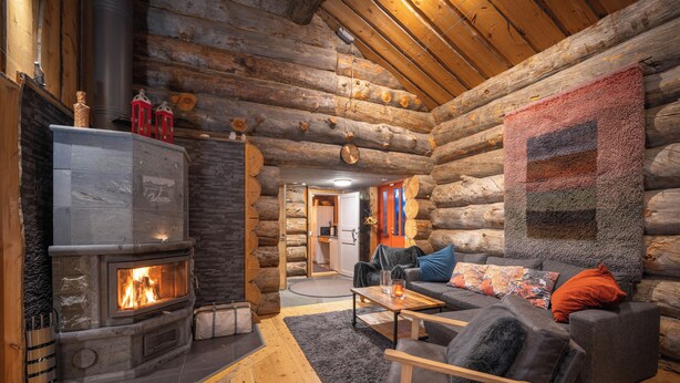 A log cabin interior with a stone fireplace, a sofa, and a quilted wall hanging. - Kuukkeli Hirvas Suite (Saariselka)