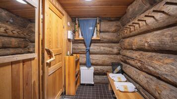 A log cabin bathroom with wooden walls, a wooden bench, a radiator, and a window with a blue curtain.