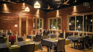 Um restaurante com paredes de tijolo, janelas amplas e mesas decoradas com toalhas listradas e velas.
