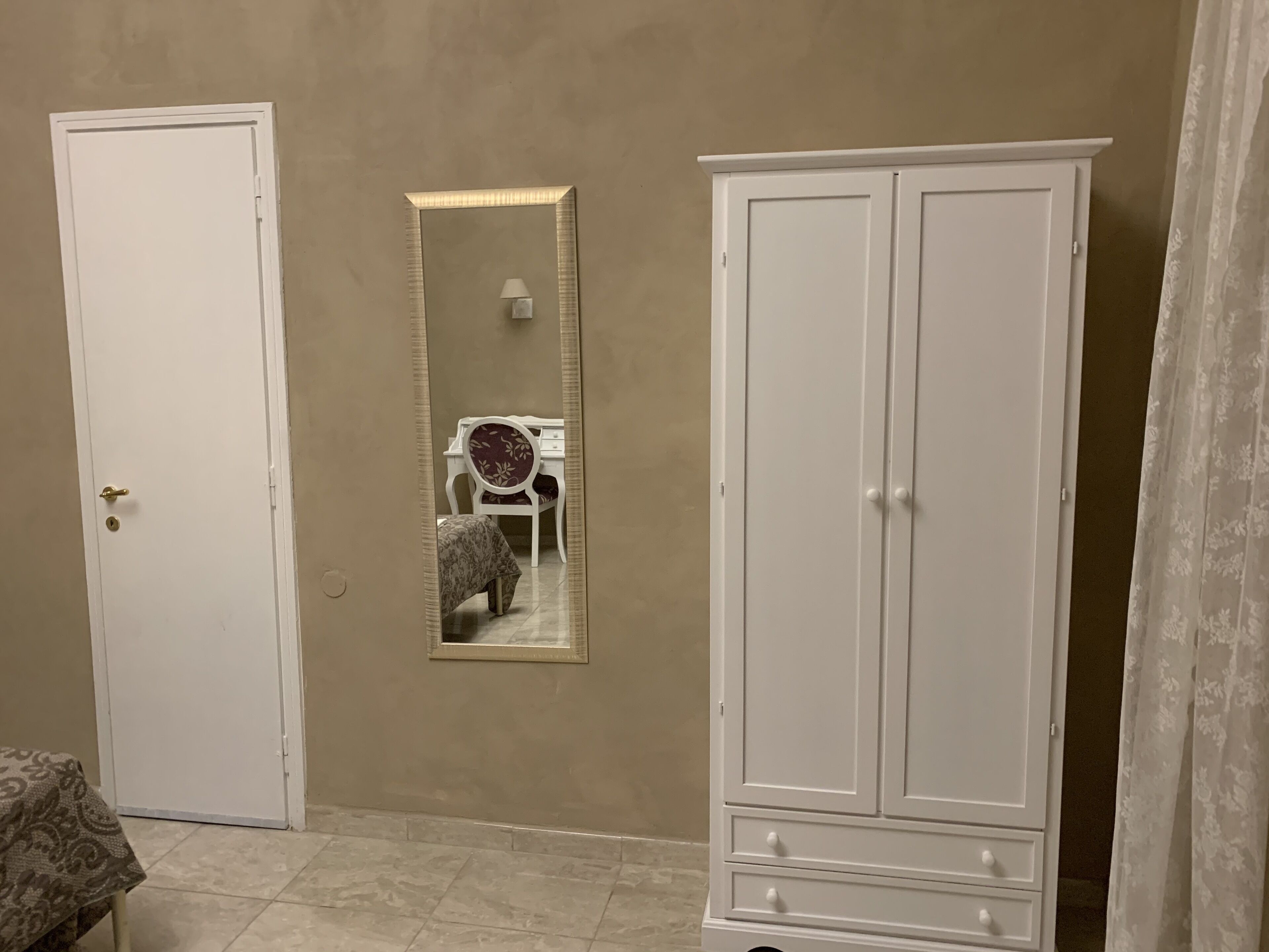 Ein Zimmer mit einer weißen Tür, einem Spiegel, einem weißen Schrank und einem Tisch mit Muster.