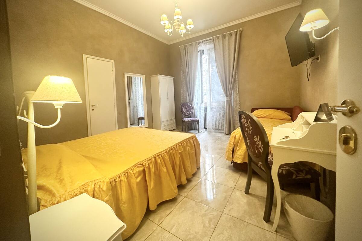 Ein Hotelzimmer mit Bett, Schreibtisch, Stuhl, Kleiderschrank, Fernseher und einem Fenster mit Vorhängen.