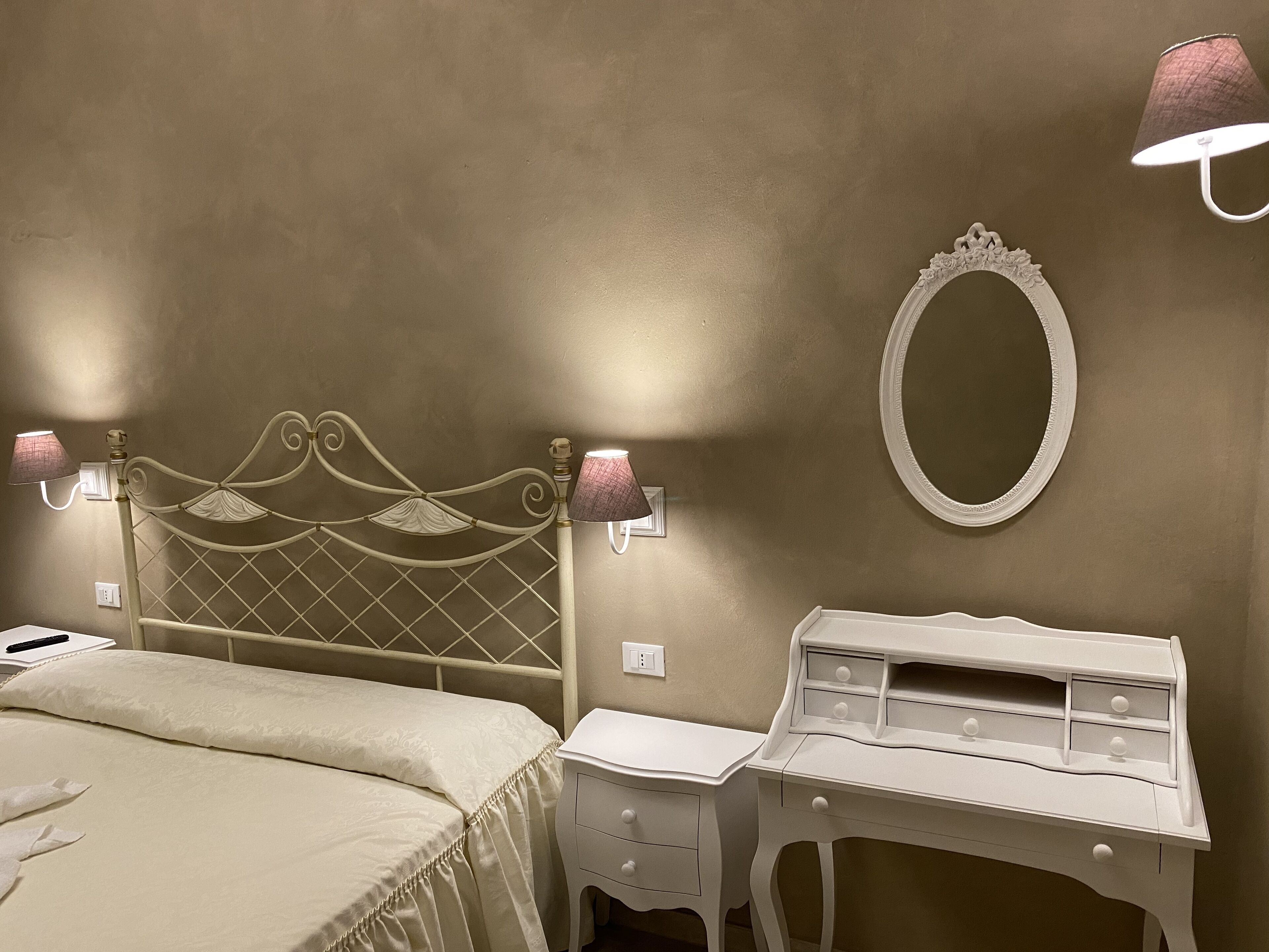 Un dormitorio con cama, mesita de noche, cómoda, espejo montado en la pared y dos apliques.