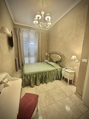 Une chambre à coucher comprenant un lit, une table de chevet, une chaise, un bureau, une lampe, un téléviseur et un lustre.