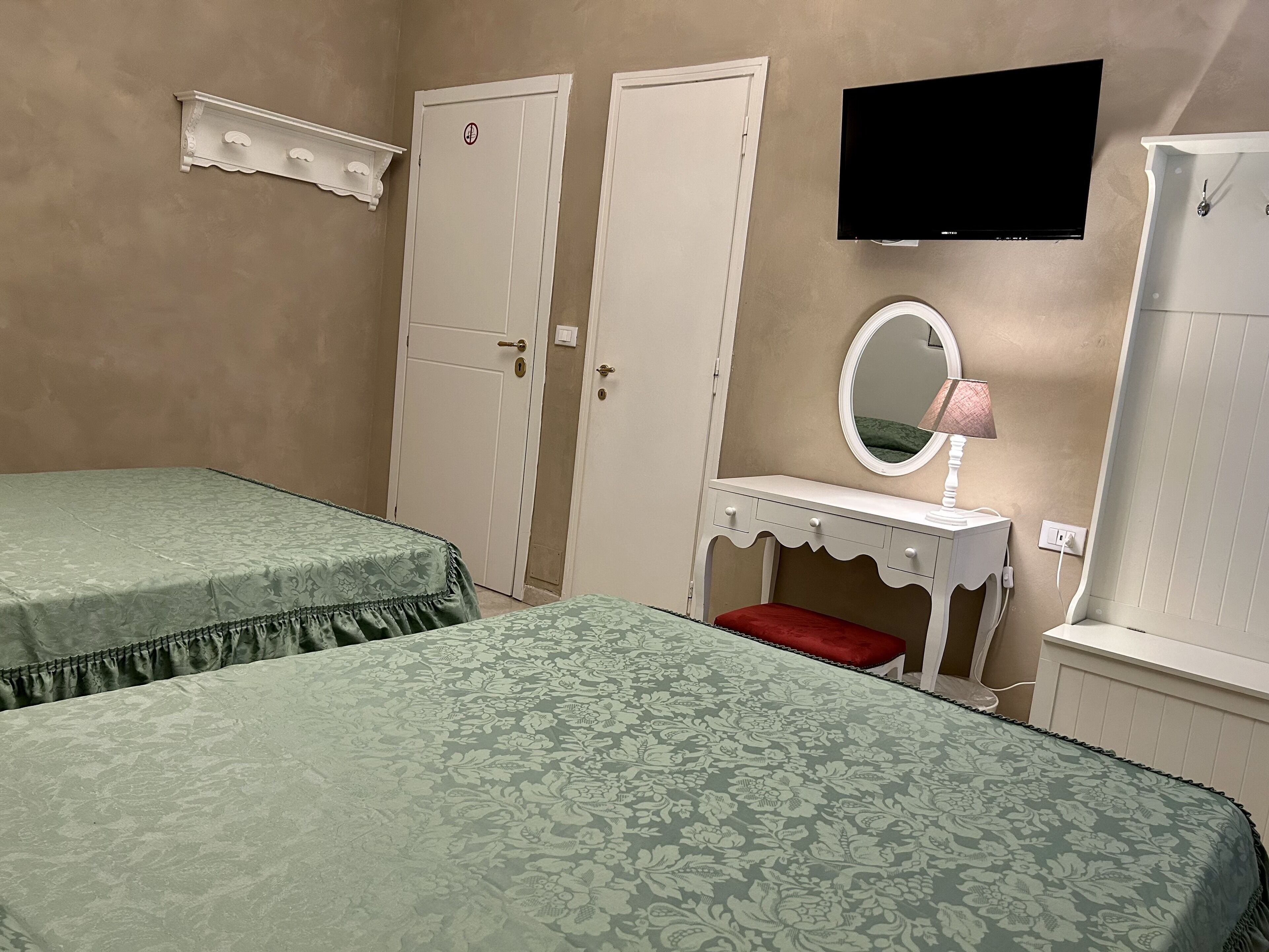 Un dormitorio con dos camas, un tocador con espejo, un televisor y dos puertas.