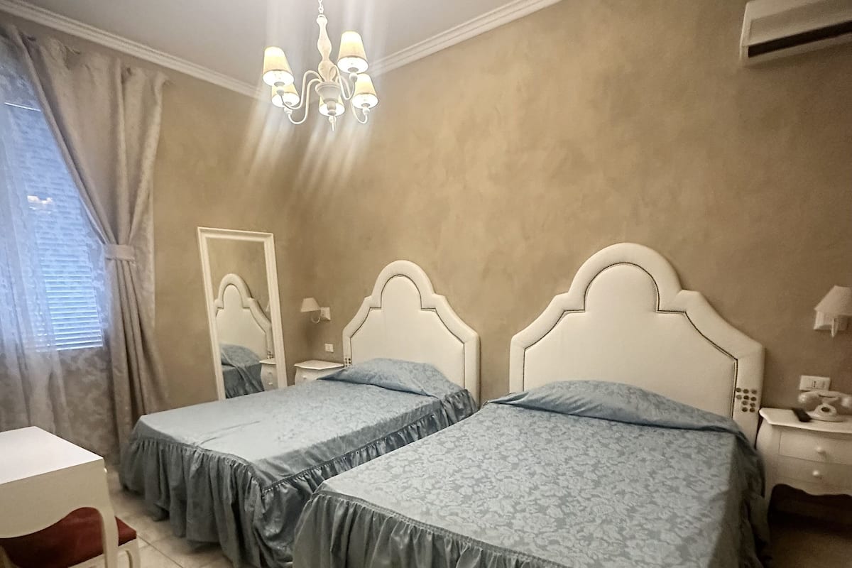 Ein Schlafzimmer mit zwei Betten, einem Schreibtisch, einem Stuhl, einem Spiegel und einer Kandelaber.