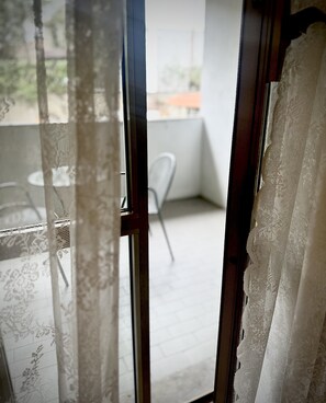 Une vue à travers une fenêtre ornée de rideaux en dentelle, avec une chaise blanche et une table à l’extérieur.