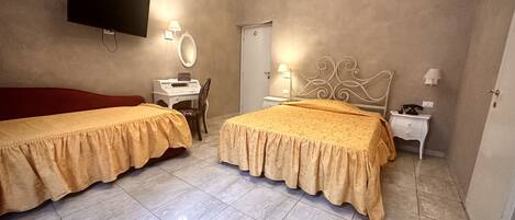 Une chambre d’hôtel avec deux lits, un bureau avec un ordinateur, un téléviseur fixé au mur, un miroir et une porte.