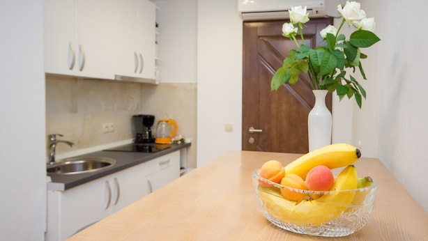 Een keuken met witte kastjes, een houten deur en een schaal fruit op een tafel.