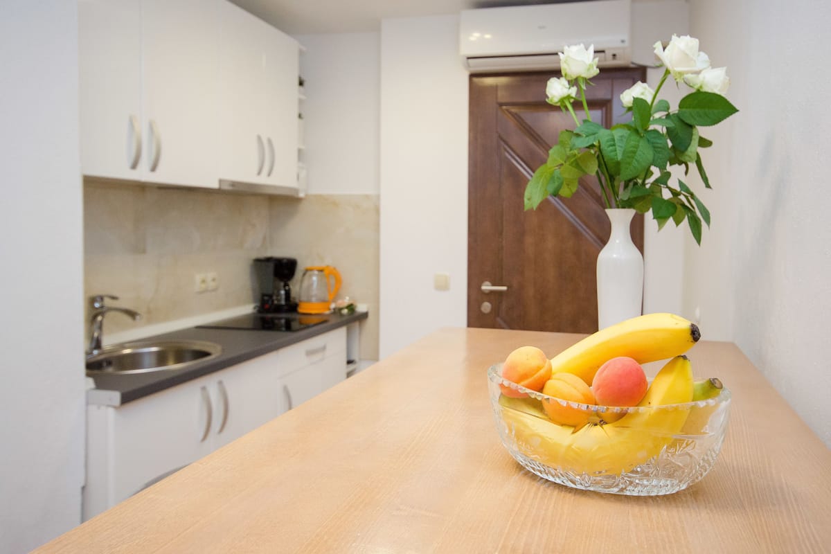 Una cocina con armarios blancos, una puerta de madera y un cuenco de frutas sobre una mesa.