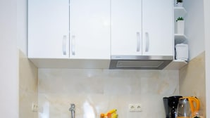 Een kleine keuken met witte kastjes, een roestvrijstalen afzuigkap en een aanrecht met een fruitmand en een koffiezetapparaat.