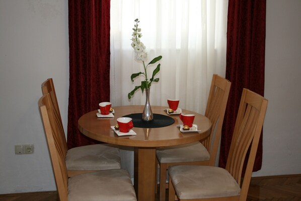 Una mesa redonda de madera con cuatro sillas, un florero con una flor blanca y tazas rojas sobre una bandeja blanca.