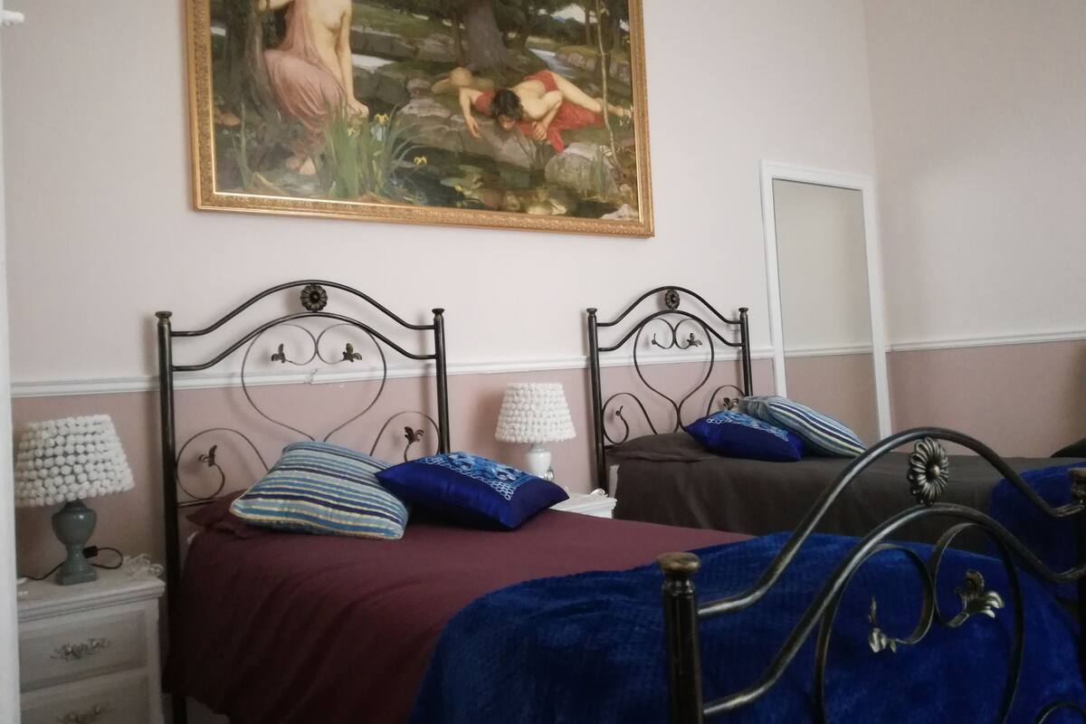 A bedroom with two beds, a painting on the wall, and a bedside table with a lamp.