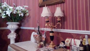 Une pièce dont les murs sont recouverts d’un papier peint à rayures, ornée d’un tableau, d’un vase rempli de fleurs et d’une table sur laquelle se trouvent divers objets, notamment des bouteilles et des boîtes.