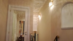 Un escalier avec une rampe, une porte ornée d’un panneau de verre décoratif et des appliques murales.