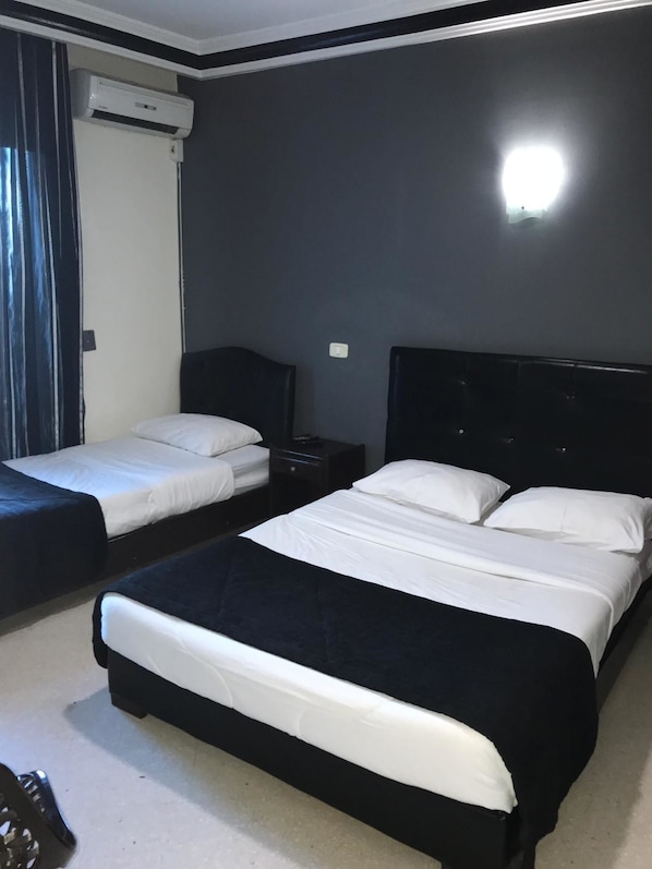 Una habitación de hotel con dos camas individuales, un cabecero oscuro, un equipo de aire acondicionado blanco y una mesita de noche pequeña.