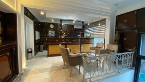 A spacious lobby with a reception desk, seating area, and a large window with blinds. - Hôtel Le Calife (Tunis)