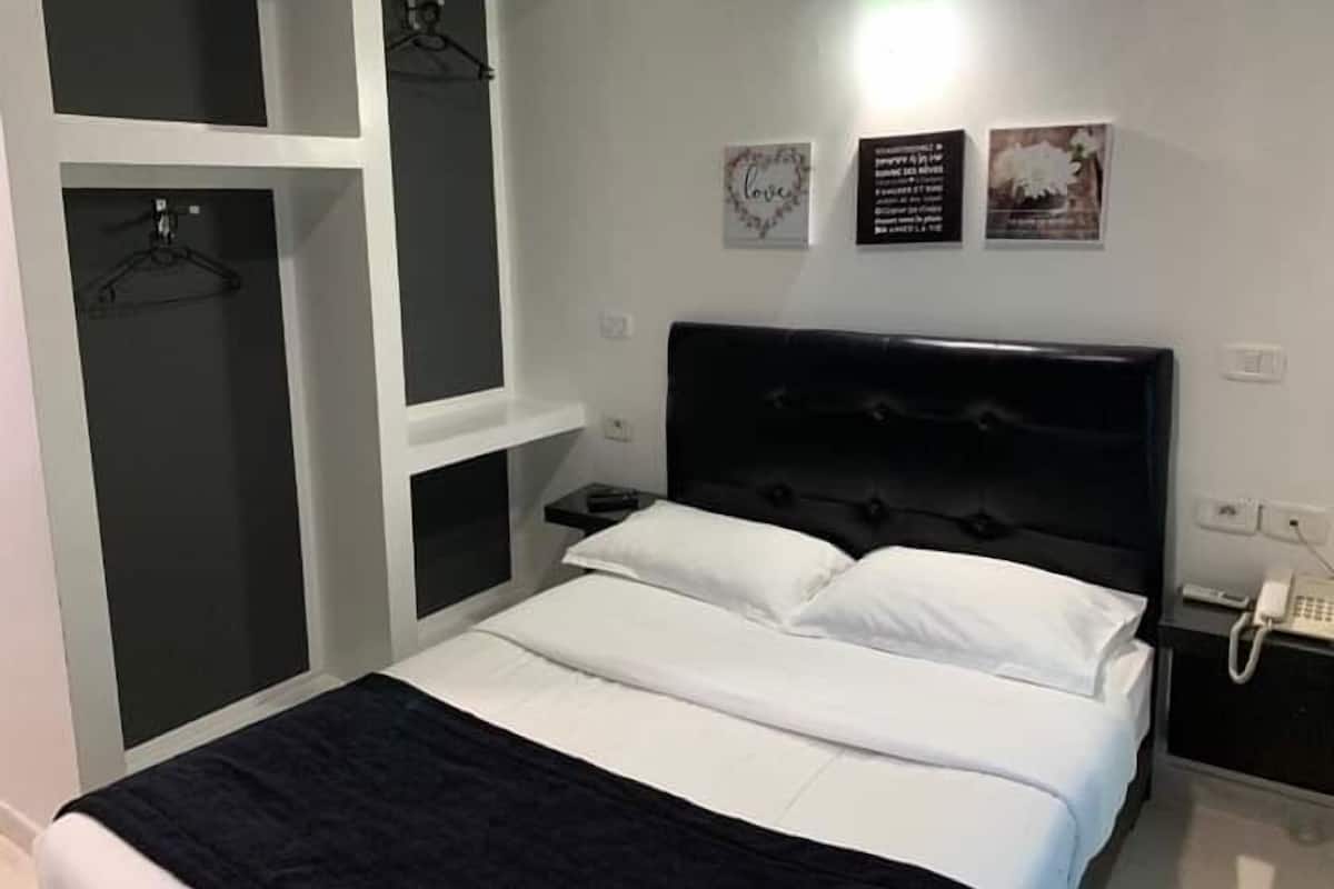 A bedroom with a bed, a bedside table, a phone, and a wall-mounted shelf with a coat rack.