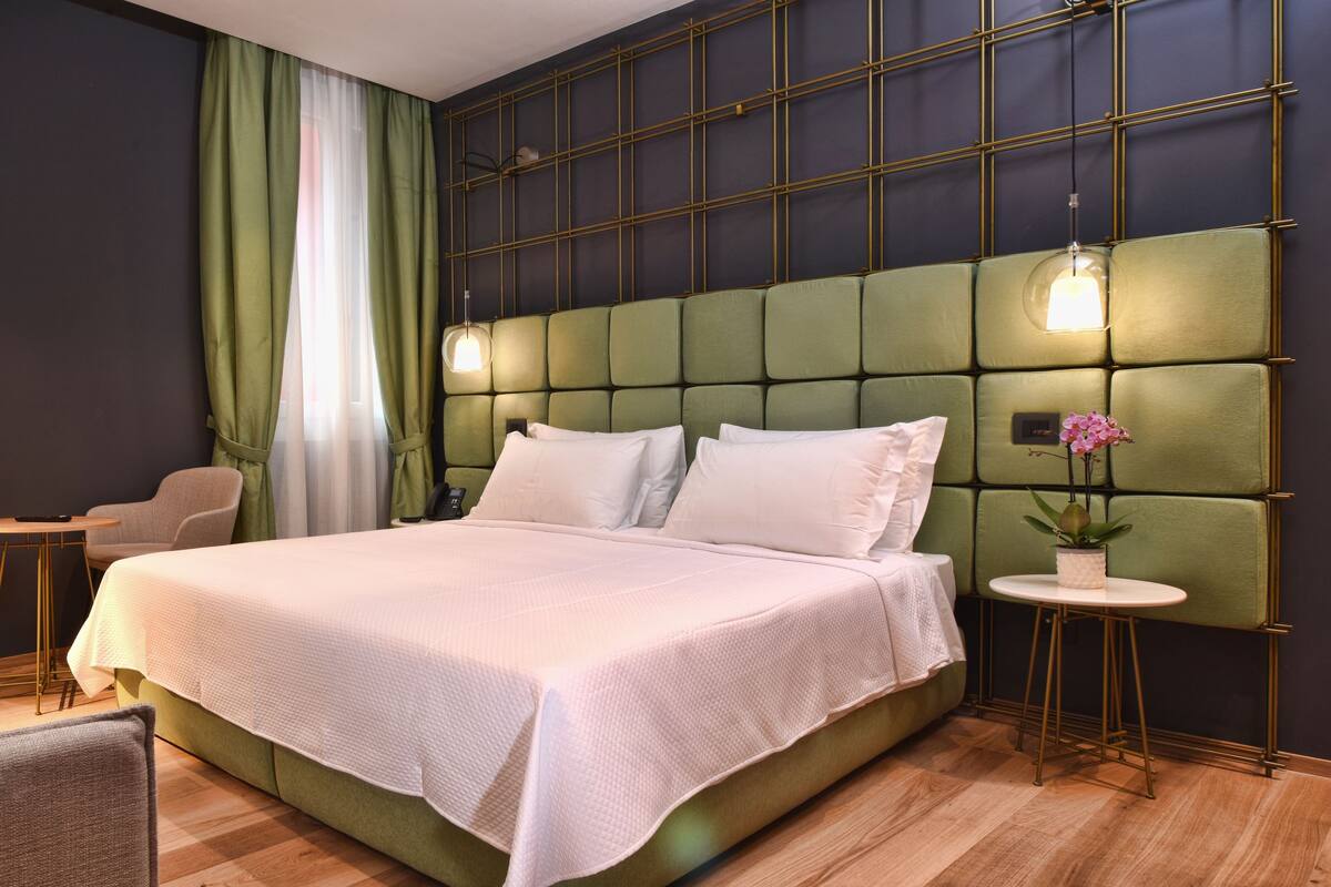 A modern hotel room with a large bed, a sofa, a small table, and a green accent wall.