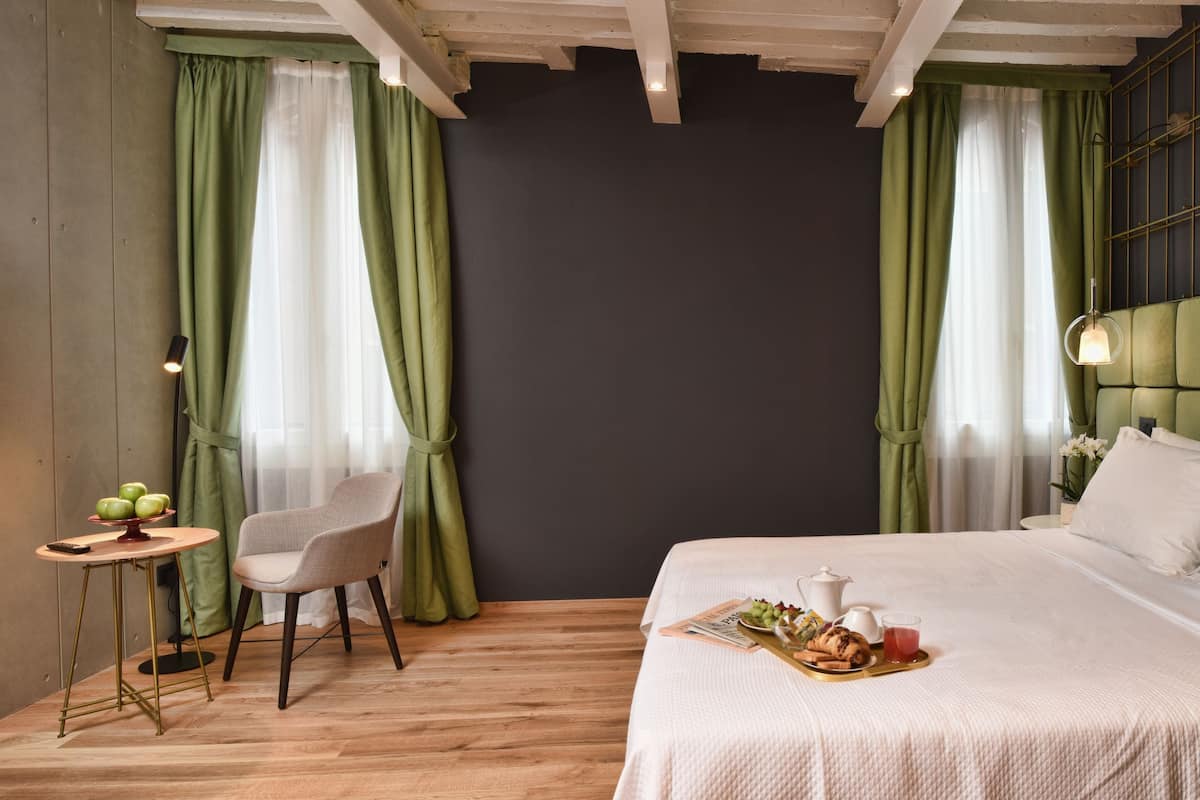 A modern hotel room with a large bed, a small table with breakfast, and a television on the wall.