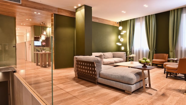 A modern hotel room with a sofa, armchair, and a small table with apples. There is a mirror, a wooden floor, and a green wall. - Hotel Maison Ducal (Venice)