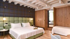 A modern hotel room with a green upholstered headboard, a wooden wardrobe, a small round table with apples, and a separate bed with a wooden headboard. - Hotel Maison Ducal (Venice)