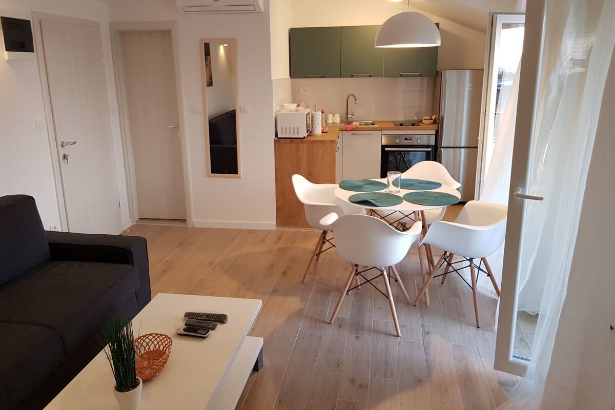 A modern living room with a sofa, a coffee table with remotes, and a dining area with a table and chairs.