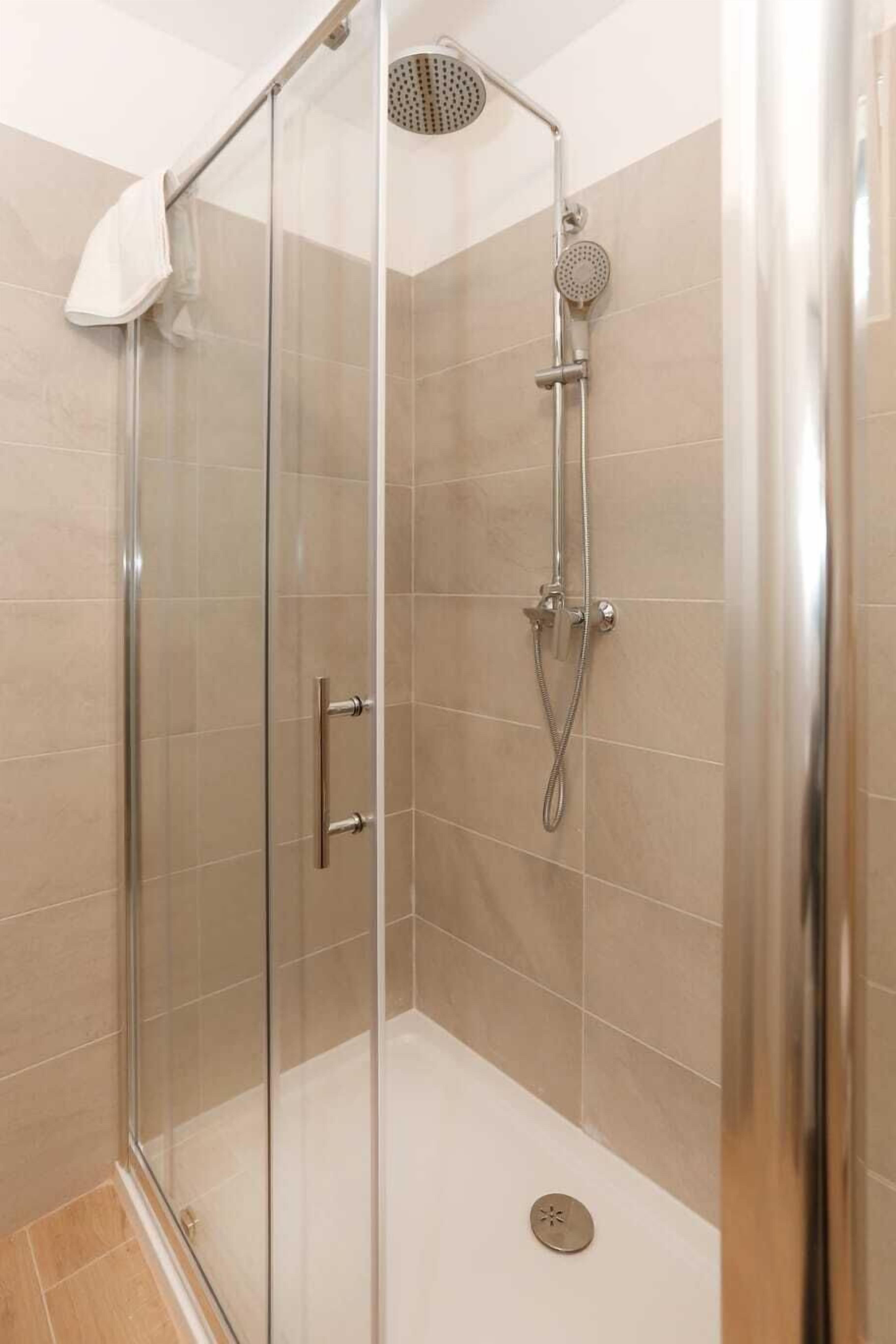 A glass-enclosed shower stall with a handheld showerhead and a wall-mounted rain showerhead.