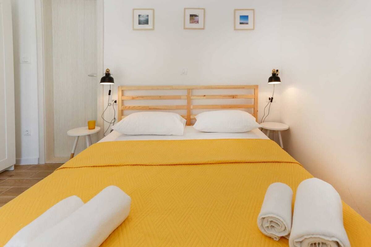A hotel room with a bed, two bedside tables, a wooden headboard, and three framed pictures on the wall.