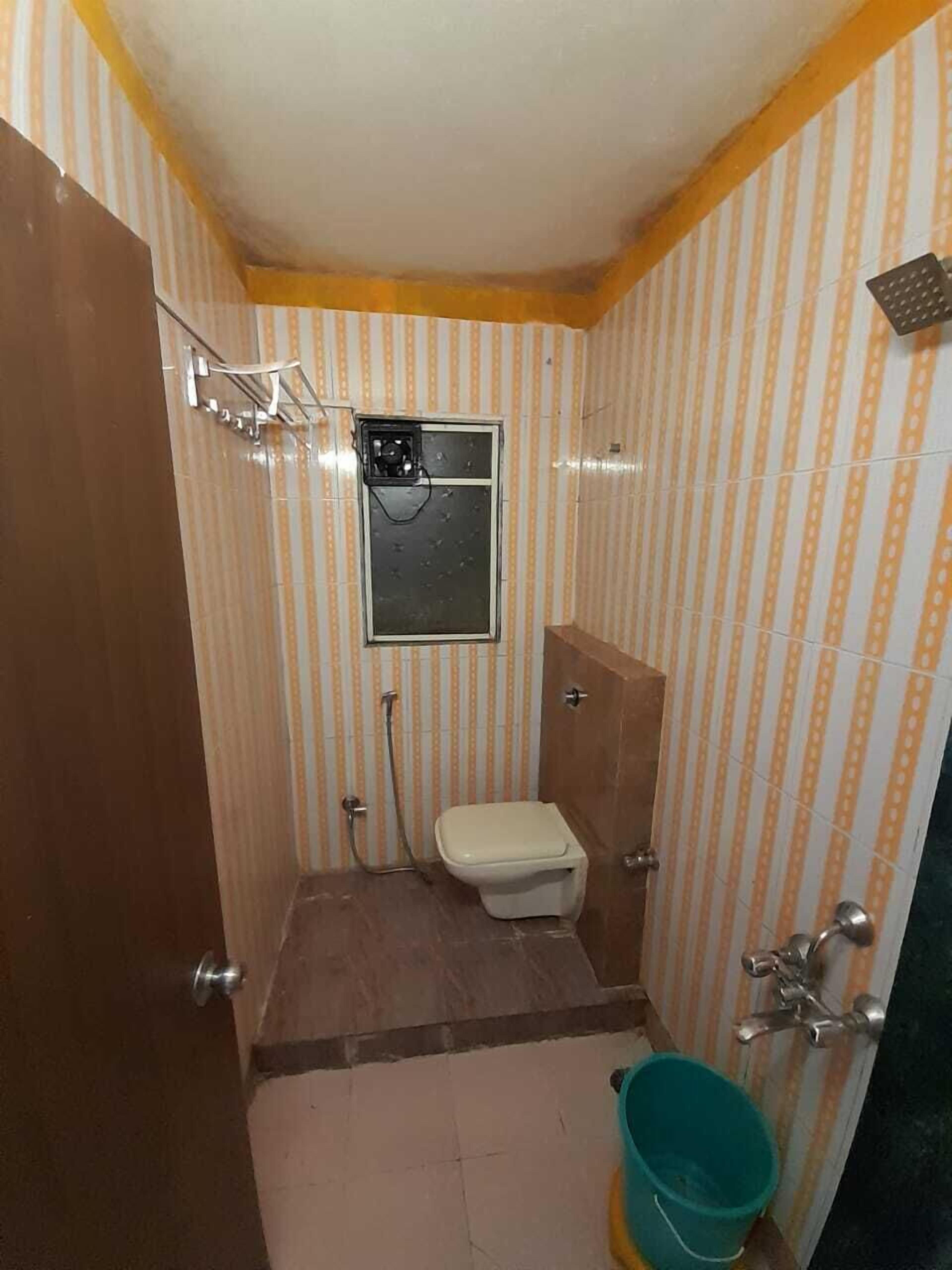 Une petite salle de bain avec des murs à rayures, des toilettes, une douche et un seau.