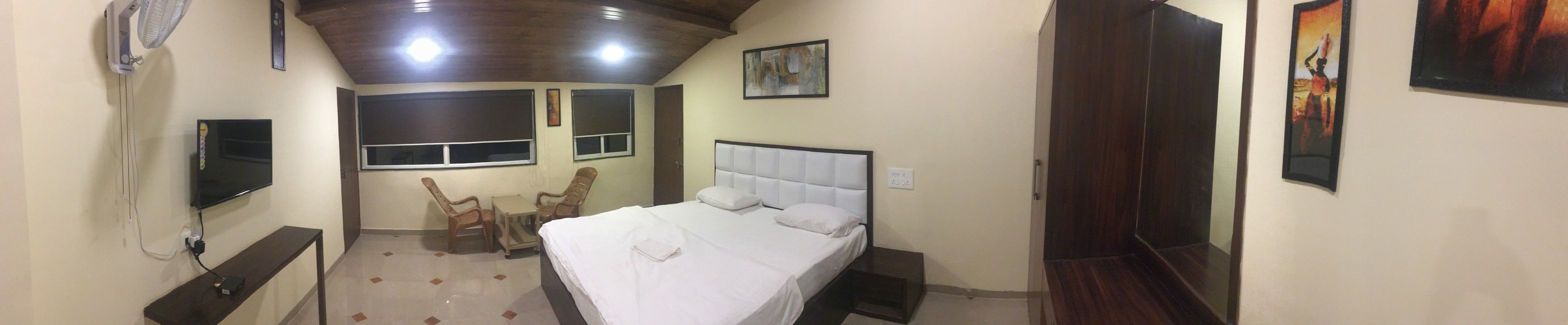 Una camera da letto con un letto, una scrivania, due sedie, una TV e opere d'arte alle pareti.