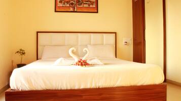 A neatly made bed with a white bedspread and two swan-shaped pillows, a small potted plant, and a painting on the wall.