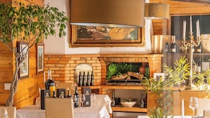 A restaurant with white tablecloths, a brick fireplace, and wine bottles on the counter. - Luxury Guest House Opus One (Faro)