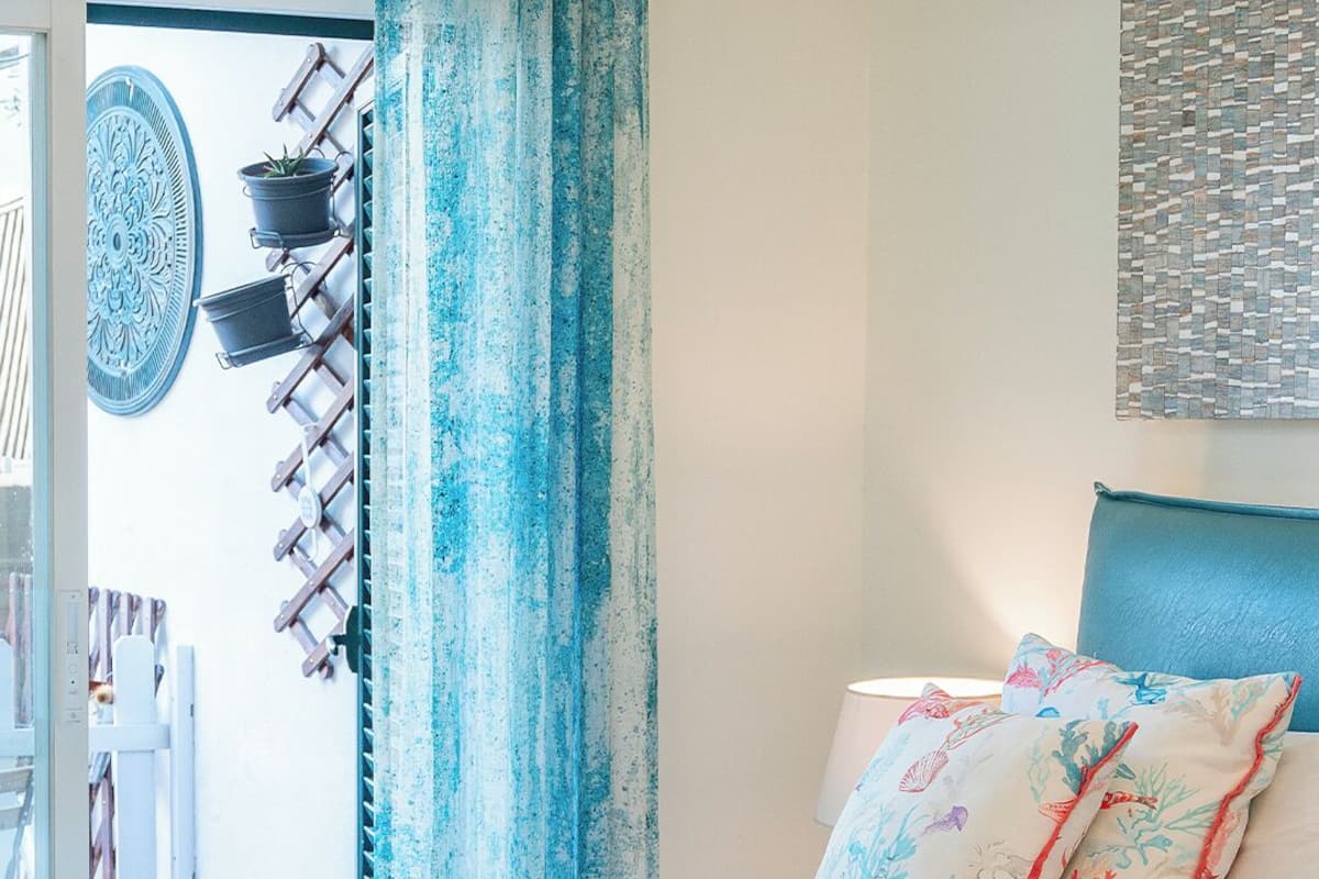 A bedroom with a bed, a headboard, a wall-mounted artwork, and a window with curtains.