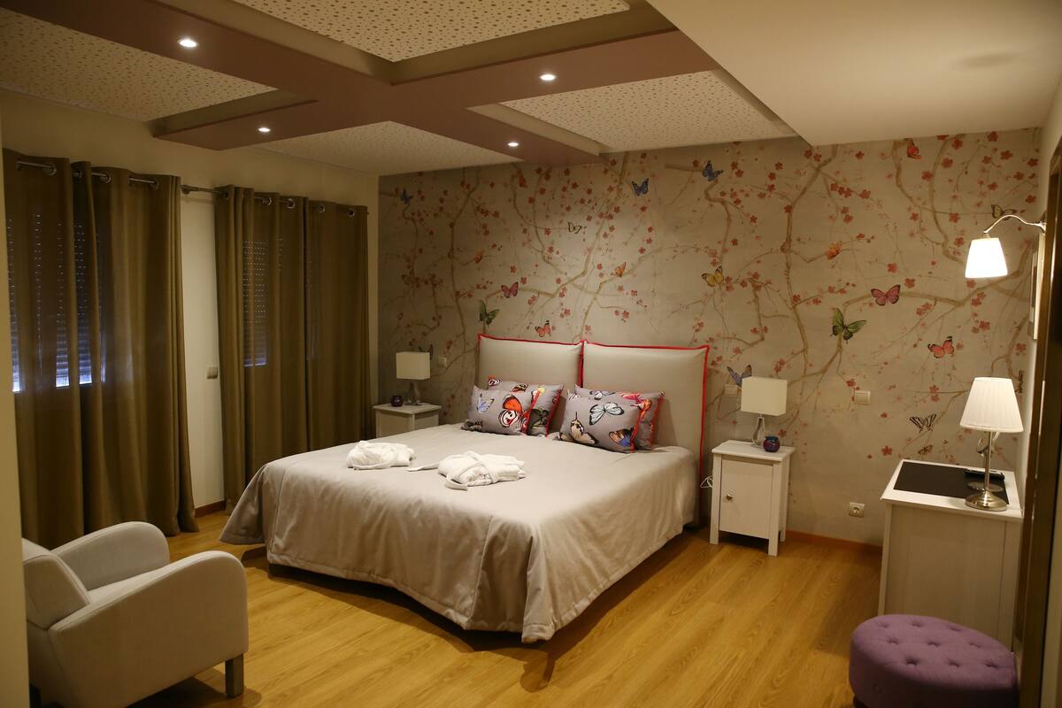 A bedroom with a large bed, two bedside tables, a chair, and a desk with a lamp.