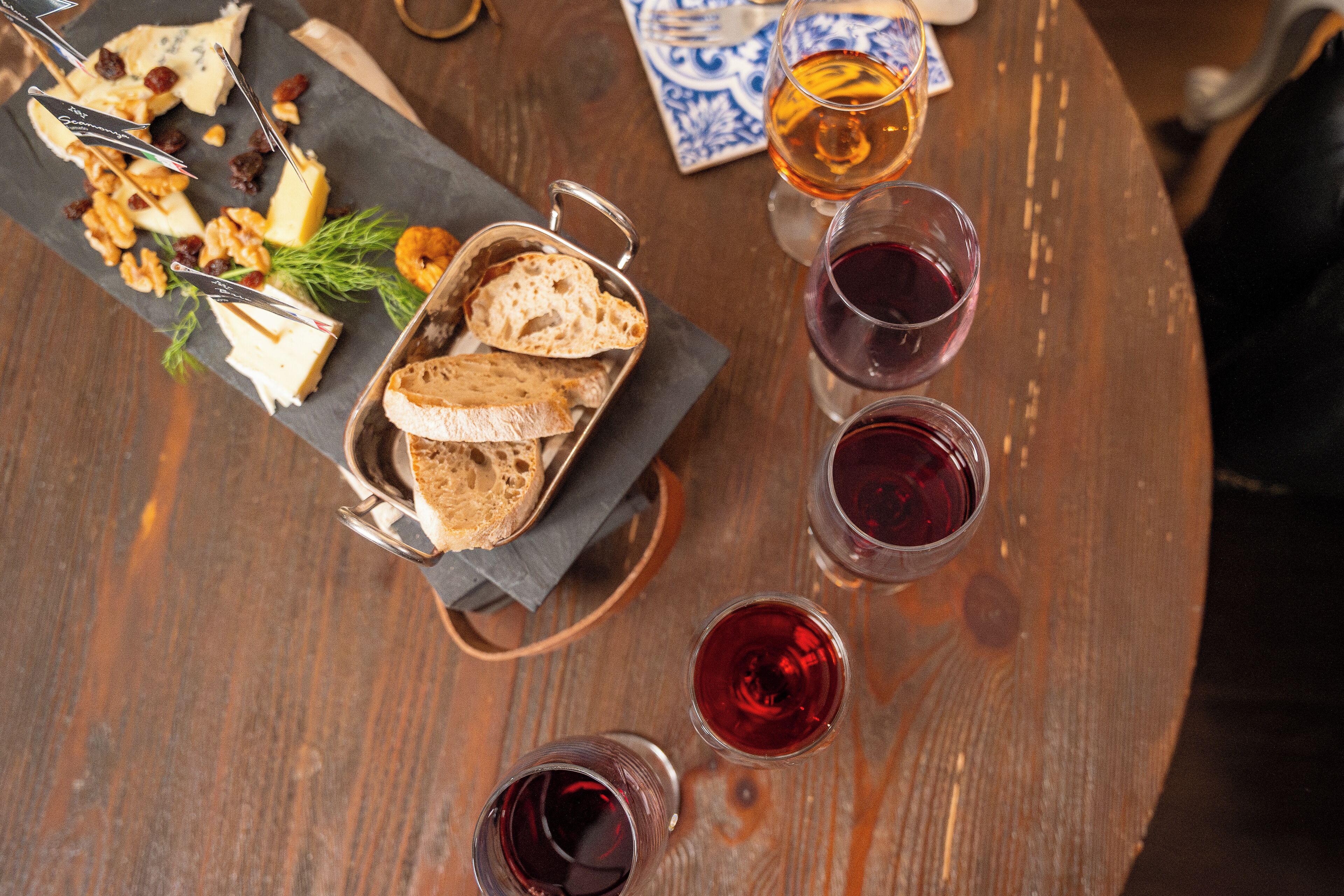 Una mesa de madera con una tabla de quesos, pan y copas de vino.