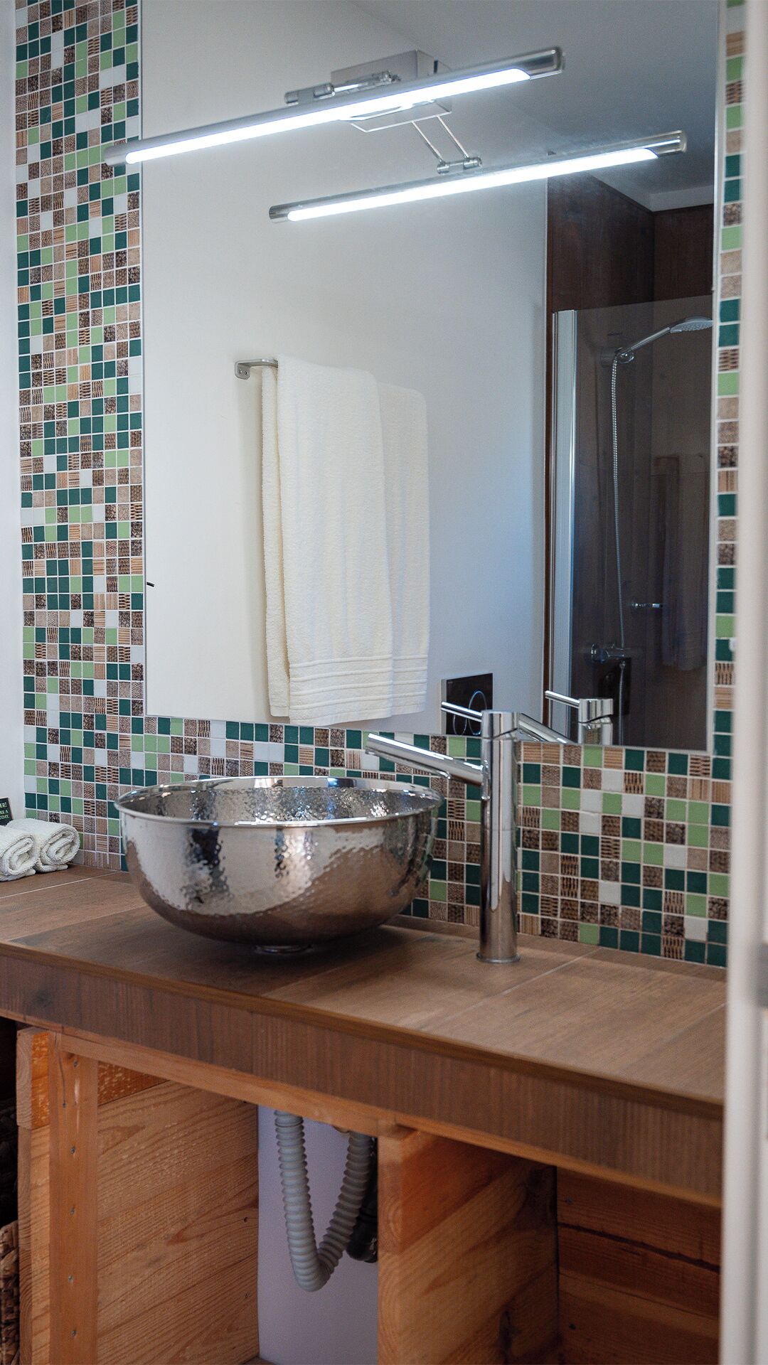 A bathroom with a wooden vanity, a large mirror, a sink with a metallic basin, and a shower area.