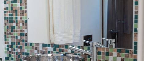A bathroom with a wooden vanity, a large mirror, a sink with a metallic basin, and a shower area.