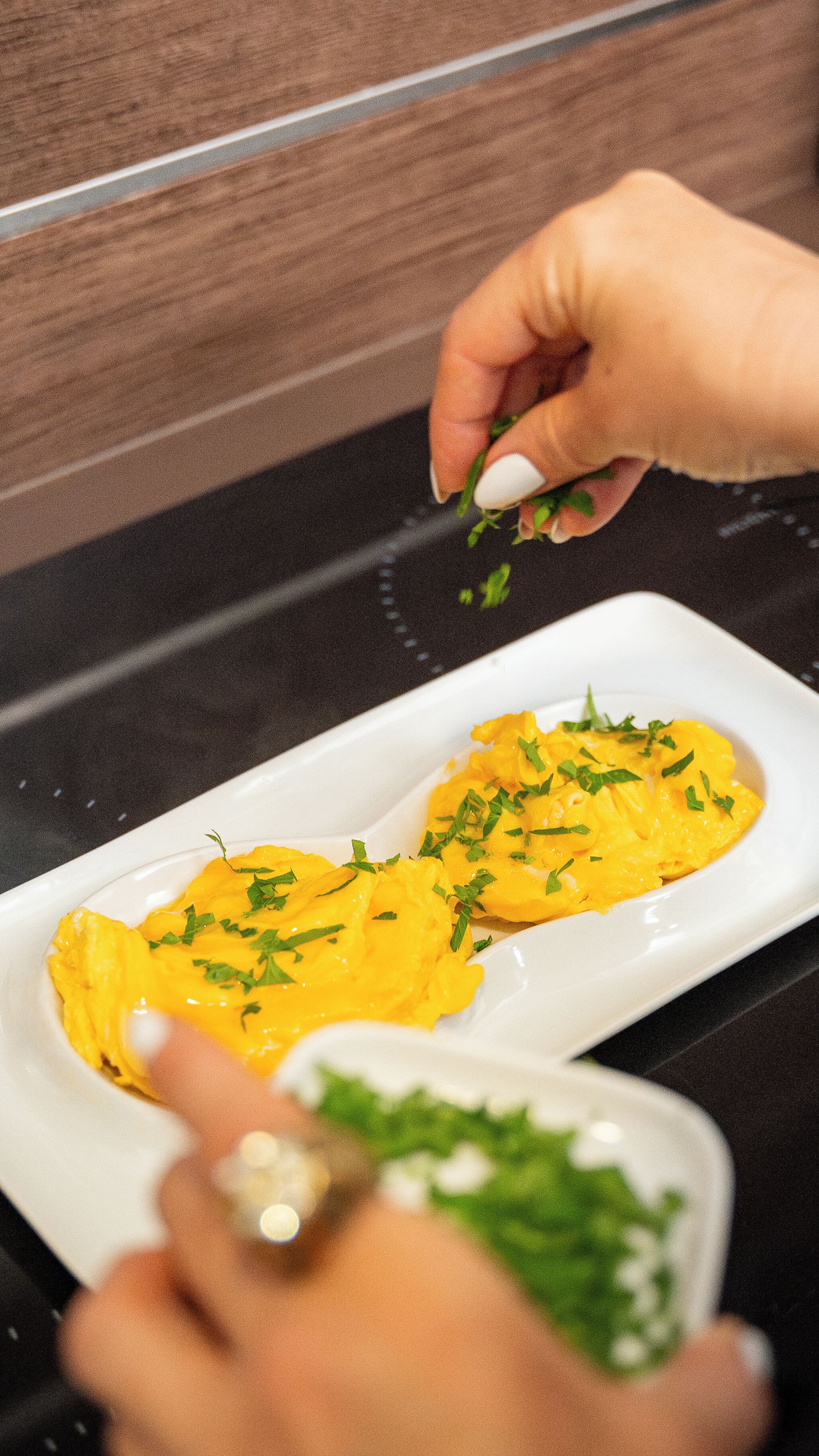 A person garnishing a dish with green herbs.
