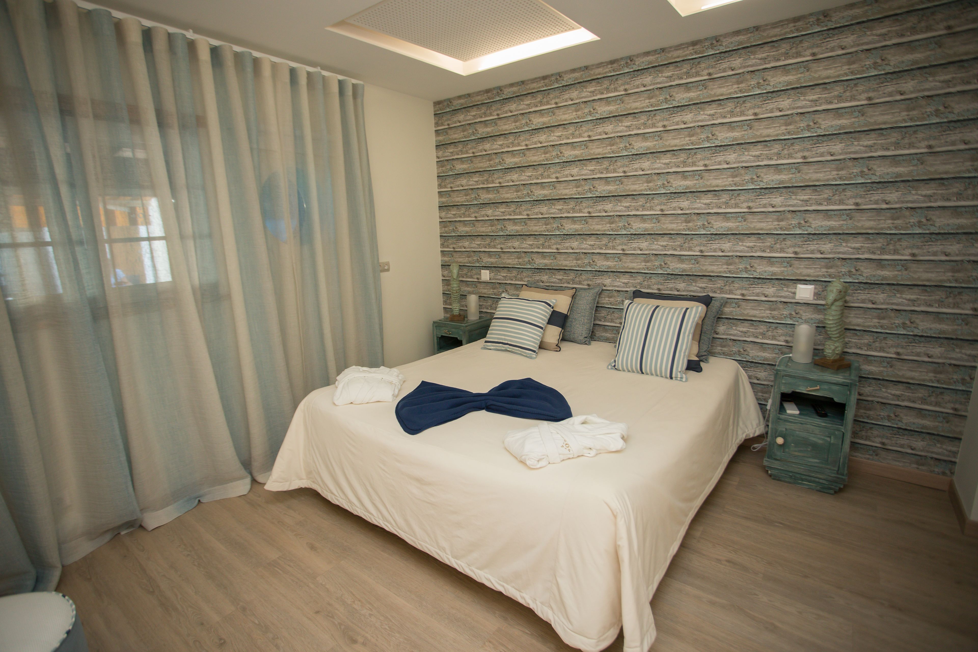 Een net opgemaakt bed met kussens en een strik, een houten wand en een nachtkastje met een lamp.