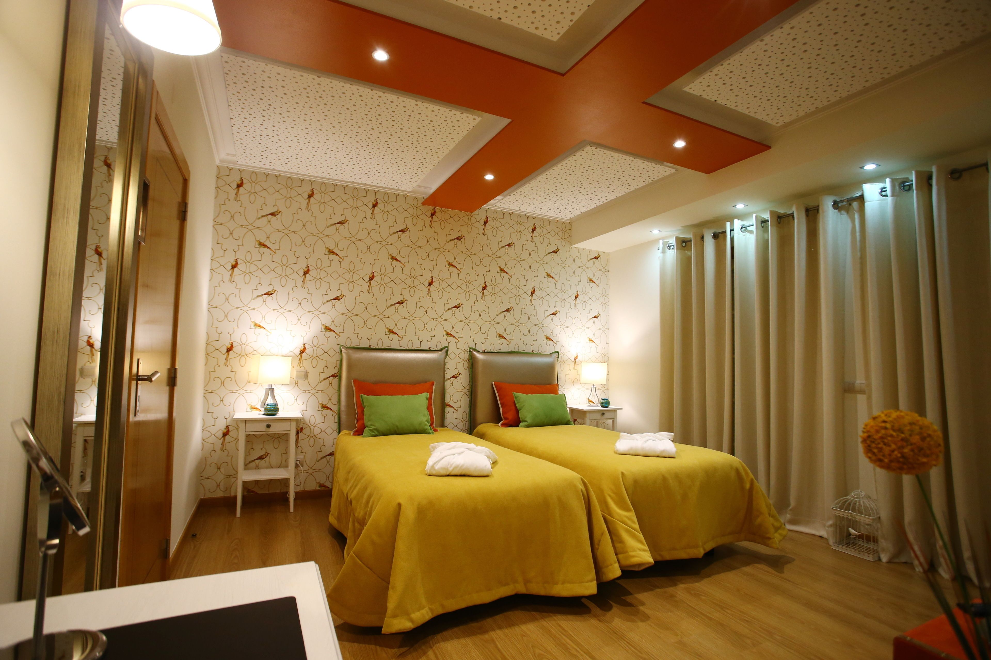A hotel room with two beds, a small bedside table with a lamp, a mirror, and a window with curtains.