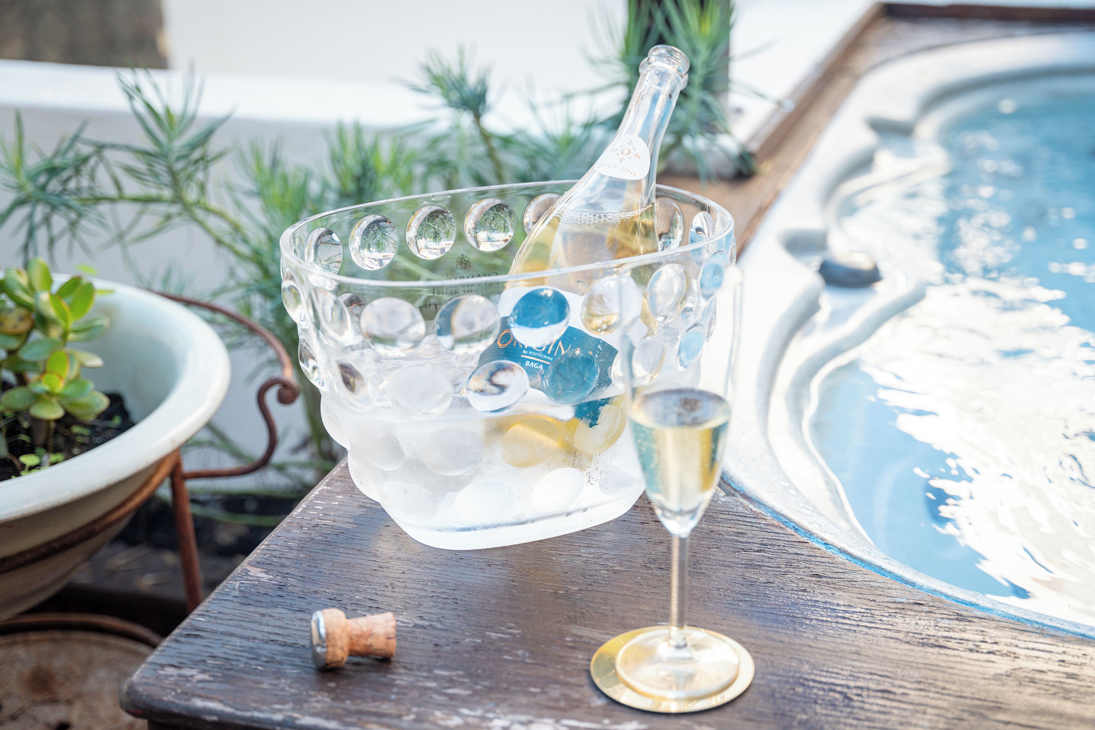 Eine Glaskugel mit Eiswürfeln und eine Champagnerflasche, daneben ein Champagnerglas.