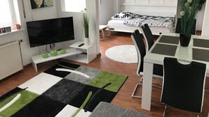 Una sala de estar moderna con una televisión de pantalla plana, una mesa de comedor con sillas, un sofá, una mesa de centro y un ventanal grande.