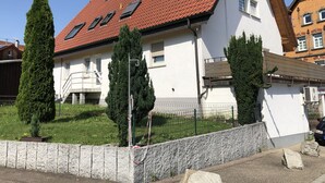 Un edificio blanco con tejido rojo, una pared de piedra y un patio cercado con dos árboles altos.