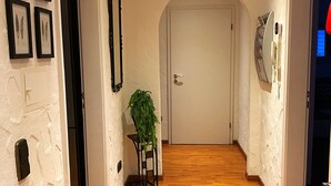 Un pasillo con suelo de madera, paredes blancas y cuadros enmarcados.