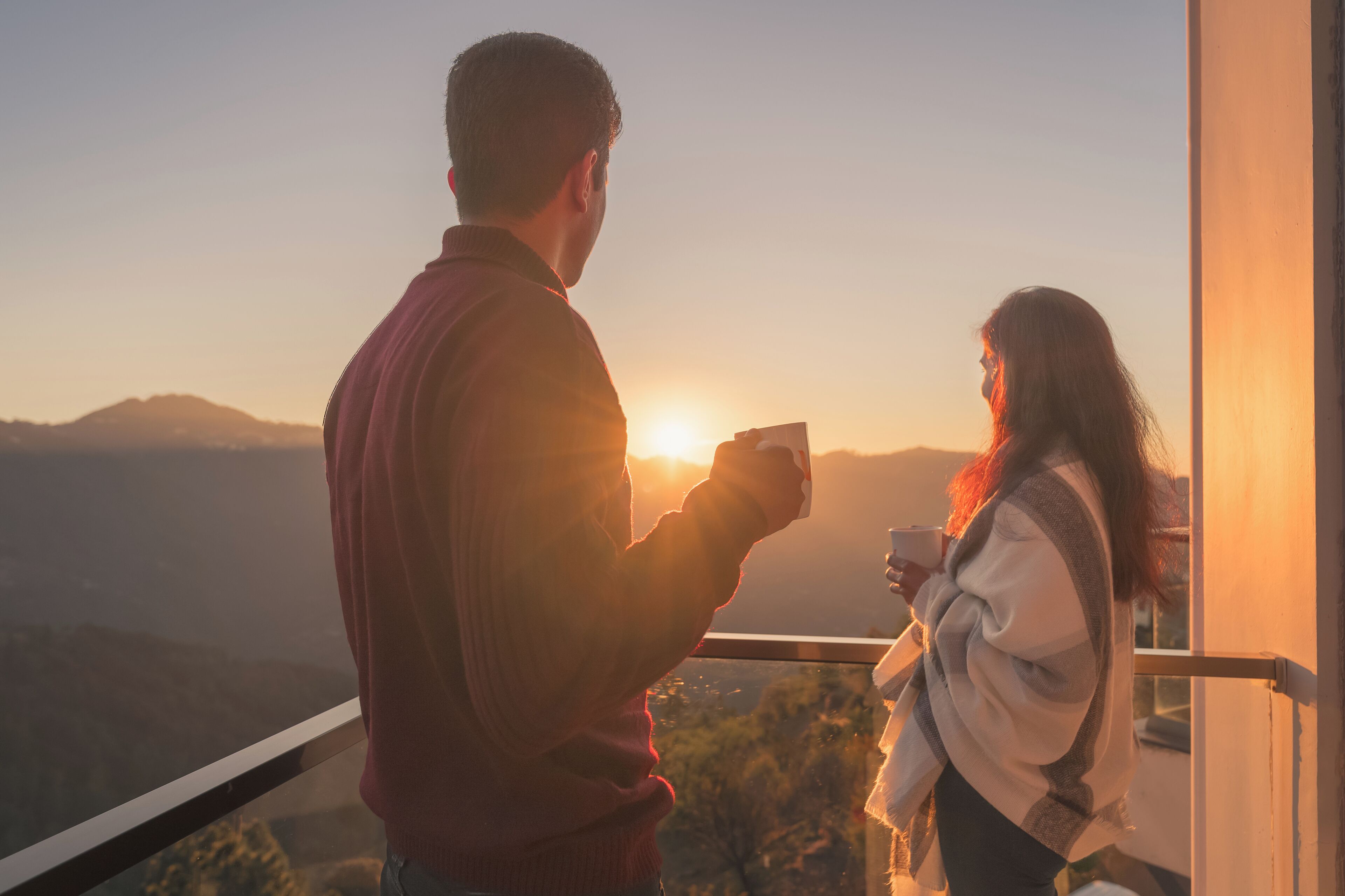 Una pareja parada junto a una ventana con vistas a un paisaje escénico al atardecer.