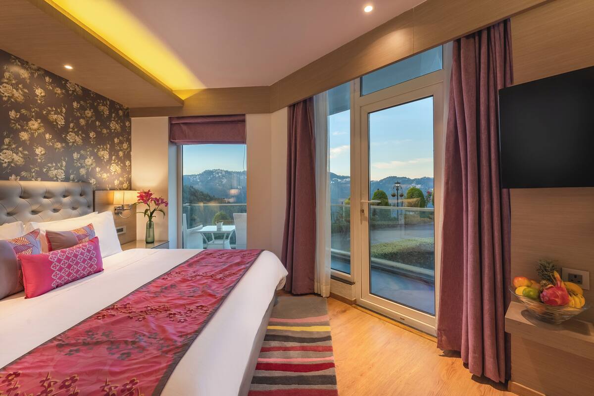 Quarto de hotel moderno com uma cama grande, varanda com vista para a cidade e televisão de tela plana.