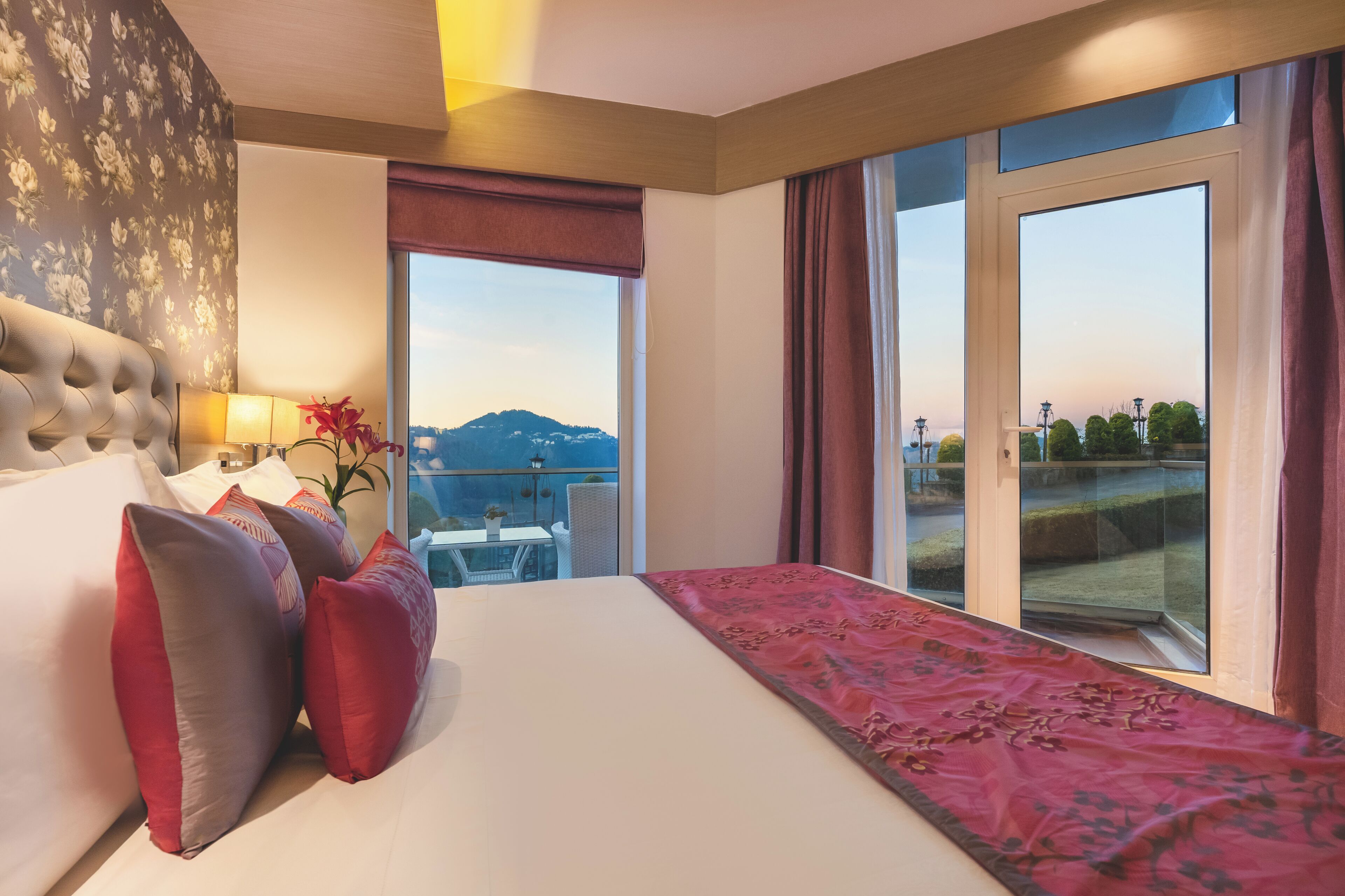 A hotel room with a large bed, a view of the outdoors, and a balcony with a table and chairs.