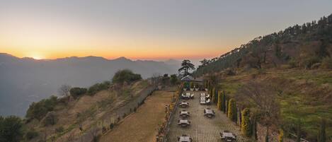 A paved terrace with outdoor seating, overlooking a hilly landscape with a sunset in the background.